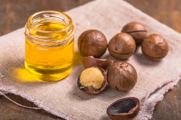 Nueces maduras de macadamia y una botella de vidrio con aceite natural — Foto de Stock