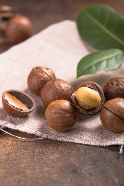 Pile noci di macadamia aperto kernel e conchiglie in sacchetto di iuta su woo — Foto Stock