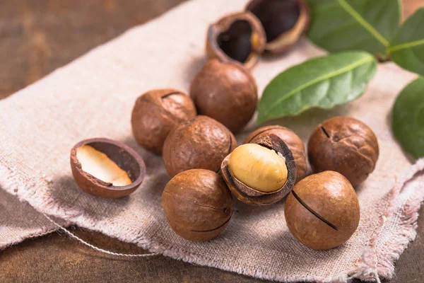 Pile noci di macadamia aperto kernel e conchiglie in sacchetto di iuta su woo — Foto Stock