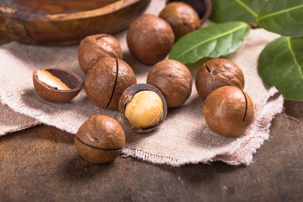 Pile noci di macadamia aperto kernel e conchiglie in sacchetto di iuta su woo — Foto Stock