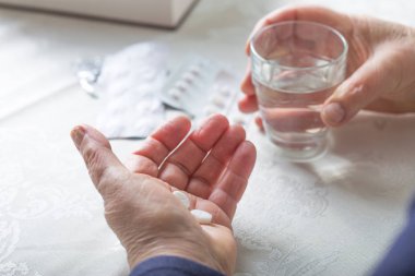 Kadın eli bir avuç dolusu farklı hap ve bir bardak su tutuyor.. 