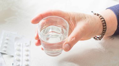 Kadın eli bir avuç dolusu farklı hap ve bir bardak su tutuyor.. 