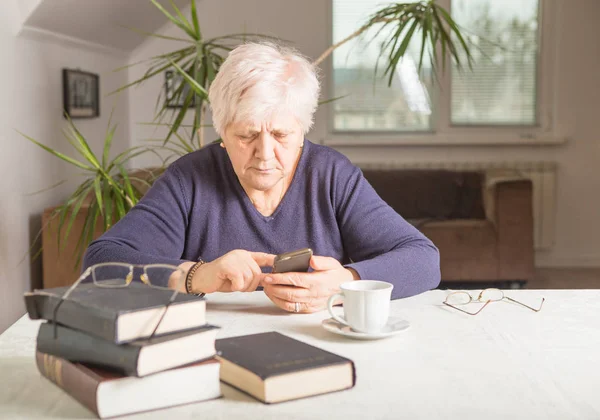 退職した女性は 居心地の良い家庭のキッチンで 携帯電話を使用しています おばあちゃんは料理にコーヒーブレイクがある 先輩はレシピを探しています インターネット上の通信 本物の瞬間 — ストック写真