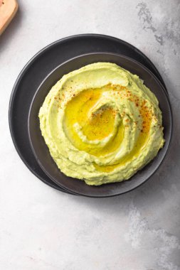 Bir kase yeşil humus, arkaplanda lezzetli nohut ve avokado kreması..