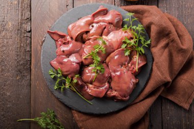 Tahta tahtada çiğ tavuk ciğeri ve ahşap arka plan. Bitki maydanozu ve biberle süslenmiş. Yiyecek malzemesi.