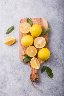 Ahşap kasede taze limonlar ve gri taş arka planda yapraklar. Taze meyve ve dilimlenmiş düzlük. Citrus arkaplanı, kopyalama alanı