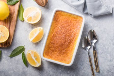 Ev yapımı güveç, puding, cheesecake, turta, turta ya da krema. Taze limon ve gri taşlı arka planda yapraklar. Meyveler ve dilimler düz yerde. Citrus arkaplanı, kopyalama alanı