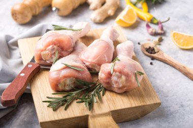 Çiğ organik tavuk bacağı ya da ahşap kesme tahtasındaki yemek malzemeleri (biber, limon, biberiye, tuz, sarımsak). Et üst görünümü