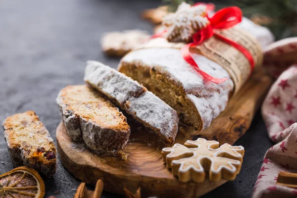 Stollen. sliced homemade Christmas dessert stollen with dried berries and nuts on stone  rustic table with cinnamon, orange slices, Christmas tree branches, gingerbread , selective focus