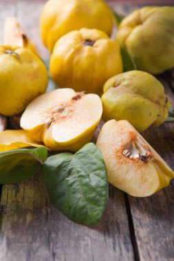 Sonbaharın sonlarında kahverengi ahşap masada olgun organik ayva meyvesi ve yeşil yaprakla dilimlenmiş. en üstteki görünüm