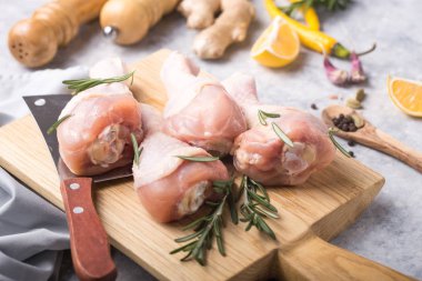 Çiğ organik tavuk bacağı ya da ahşap kesme tahtasındaki yemek malzemeleri (biber, limon, biberiye, tuz, sarımsak). Et üst görünümü