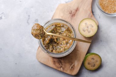 Cam bir kavanozda, tahta kesme tahtasının üzerinde şekerli, öğütülmüş yeşil feijoa. Gri arka plan. Üst Manzara. Sağlıklı beslenme malzemeleri konsepti