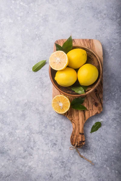 Gri taş arka planda taze limon ve yapraklar. Taze meyve ve dilimlenmiş düzlük. Citrus arkaplanı, kopyalama alanı