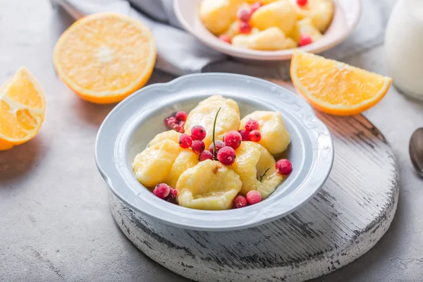 Ukrainian, Russian food, lazy vareniki; Curd or cheese gnocchi with fresh raw rcurrant, cream and mint, on a grey concrete background, copy space top view