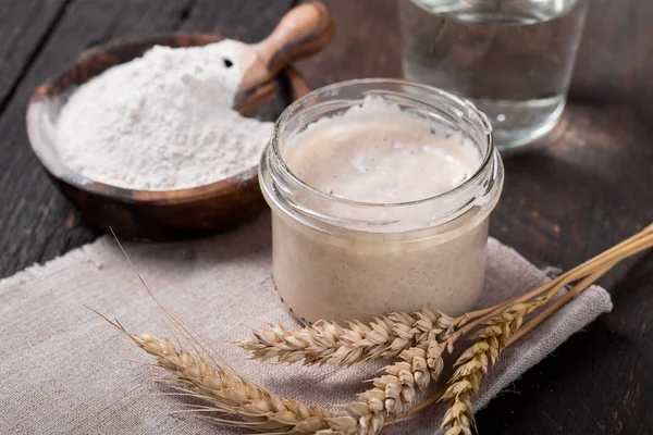 Fresh homemade bubbly sourdough starter, a fermented mixture of water and flour to use as leaven for bread baking, on wooden table