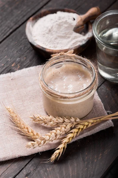 Fresh homemade bubbly sourdough starter, a fermented mixture of water and flour to use as leaven for bread baking, on wooden table