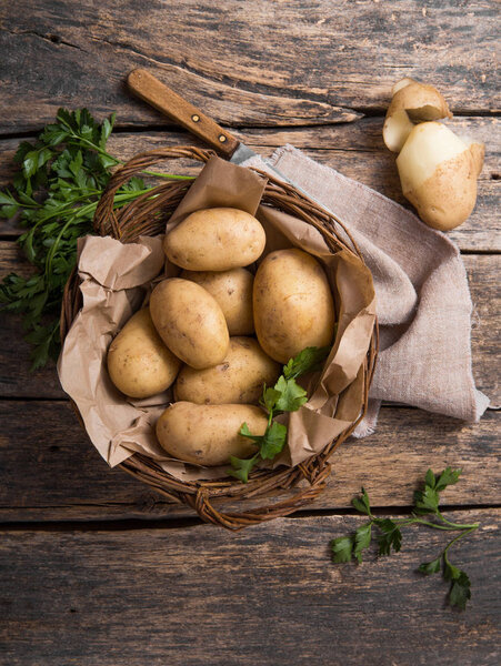 Raw organic potato with parsley  in basket on wooden table top view