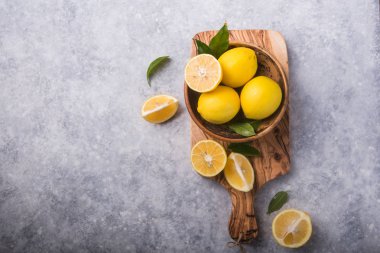 Gri taş arka planda taze limon ve yapraklar. Taze meyve ve dilimlenmiş düzlük. Citrus arkaplanı, kopyalama alanı