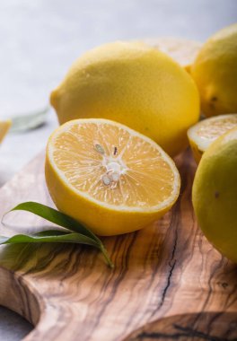 Ahşap kasede taze limonlar ve gri taş arka planda yapraklar. Taze meyve ve dilimlenmiş düzlük. Citrus arkaplanı, kopyalama alanı