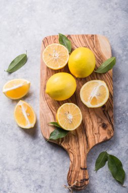 Ahşap kasede taze limonlar ve gri taş arka planda yapraklar. Taze meyve ve dilimlenmiş düzlük. Citrus arkaplanı, kopyalama alanı