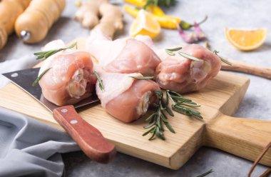 Çiğ organik tavuk bacağı ya da ahşap kesme tahtasındaki yemek malzemeleri (biber, limon, biberiye, tuz, sarımsak). Et üst görünümü