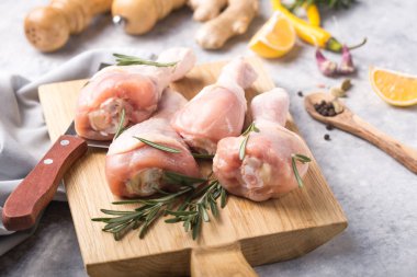 Çiğ organik tavuk bacağı ya da ahşap kesme tahtasındaki yemek malzemeleri (biber, limon, biberiye, tuz, sarımsak). Et üst görünümü