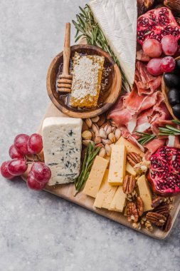 Geleneksel İtalyan antipasto tabağı. Tahta kesme tahtasında çeşitli peynirler. Brie peyniri, çedar dilimleri, gogonzola, ceviz üzümü, zeytin, prosciutto, biberiye ve bir bardak kırmızı şarap. en üstteki görünüm