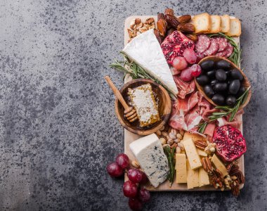 Geleneksel İtalyan antipasto tabağı. Tahta kesme tahtasında çeşitli peynirler. Brie peyniri, çedar dilimleri, gogonzola, ceviz üzümü, zeytin, prosciutto, biberiye ve bir bardak kırmızı şarap. en üstteki görünüm