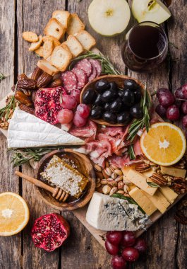 Geleneksel İtalyan antipasto tabağı. Tahta kesme tahtasında çeşitli peynirler. Brie peyniri, çedar dilimleri, gogonzola, ceviz üzümü, zeytin, prosciutto, biberiye ve bir bardak kırmızı şarap. en üstteki görünüm