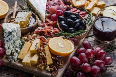 Geleneksel İtalyan antipasto tabağı. Tahta kesme tahtasında çeşitli peynirler. Brie peyniri, çedar dilimleri, gogonzola, ceviz üzümü, zeytin, prosciutto, biberiye ve bir bardak kırmızı şarap. en üstteki görünüm