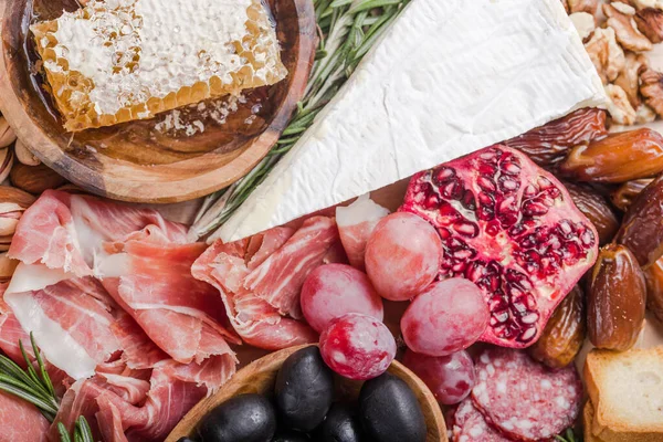 Geleneksel İtalyan antipasto tabağı. Tahta kesme tahtasında çeşitli peynirler. Brie peyniri, çedar dilimleri, gogonzola, ceviz üzümü, zeytin, prosciutto, biberiye ve bir bardak kırmızı şarap. en üstteki görünüm