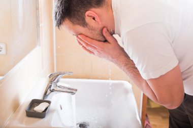 Yüzünü yıkayan adam lavaboda akan suyla sabunu duruluyor, Coronavirus 'un vücut hijyenini önlüyor. Covid-19 kolları temizleyerek pandemik koruma