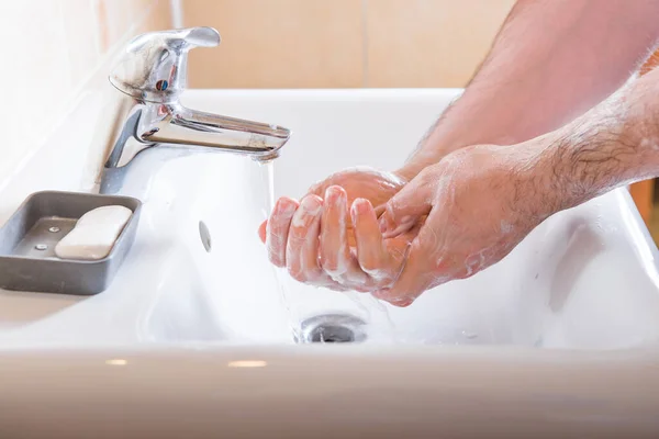 Washing hands man rinsing soap with running water at sink, Coronavirus prevention hand hygiene. Covid-19 pandemic protection by cleaning arms