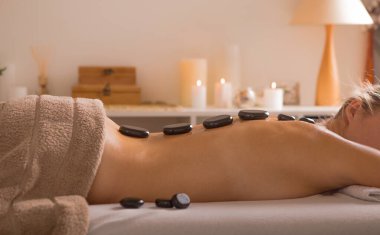 Genç bir kadın kaplıca salonunda sıcak taş masajı yaptırıyor. Güzellik tedavisi konsepti. Kız spa prosedürlerinde rahatlıyor.