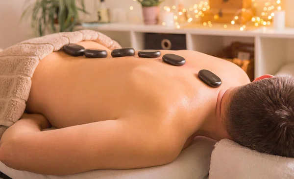 Man with stones on massage table at spa with body treatment. Person lying and relaxing during \