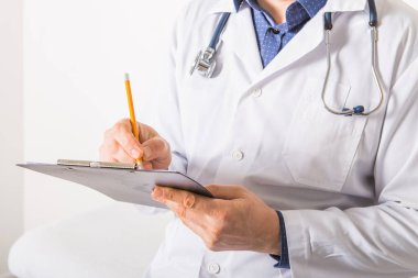 Steteskoplu bir doktor beyaz arka plandaki panoya RX reçetesi yazıyor, yakın plan. Tıbbi hizmet