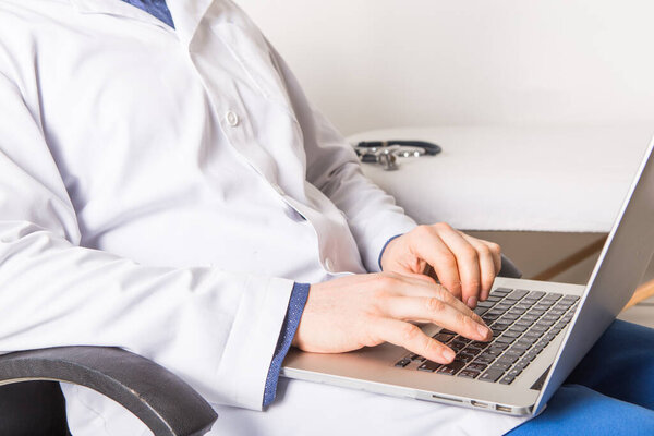 Mature doctor working on laptop and medication's cases to make prescriptions in his clinic office. Man preparing online internet prescription