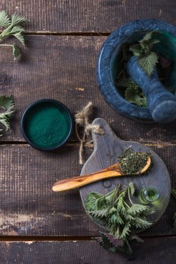 Ahşap masa üzerinde taze ısırgan otu yaprakları. Urtica dioica yağı ve spirulina tozu. Sağlık için sağlıklı bir takviye..