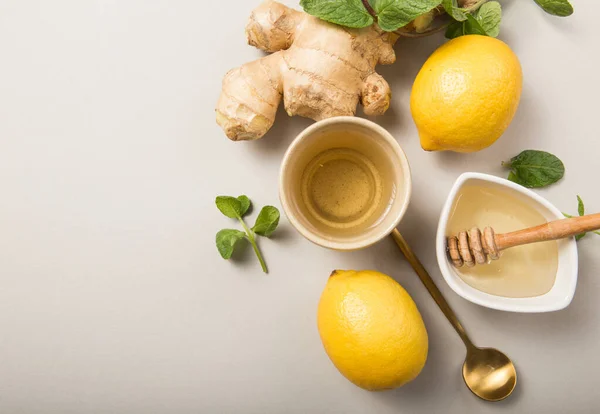 Ginger Lemon Tea with Honey. Warming immune boosting tea with citrus and ginger. Cup, honey,  ginger root on grey  pastel background, copy space, top view.