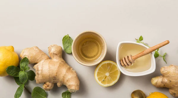 Ginger Lemon Tea with Honey. Warming immune boosting tea with citrus and ginger. Cup, honey,  ginger root on grey  pastel background, copy space, top view.