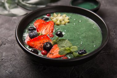 Renkli, sağlıklı yiyecekler. Acai smoothie kasesi. Keto kahvaltı fikri. Meyveli buzlu içecek, acai. Yeşil spirulinalı kahvaltı, çilek, chia, kivi siyah tabakta.