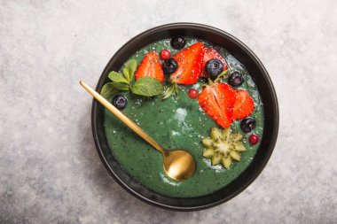 Renkli, sağlıklı yiyecekler. Acai smoothie kasesi. Keto kahvaltı fikri. Meyveli buzlu içecek, acai. Yeşil spirulinalı kahvaltı, çilek, chia, kivi siyah tabakta.