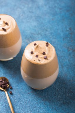 Dalgona Köpüklü Kahve, mavi beton masanın üzerinde çırpılmış kahve, şeker ve süt bulunan bir Güney Kore içeceğidir.