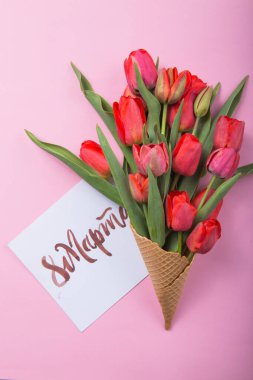 Dondurmalı waffle külahında kırmızı güzel laleler ve renkli arka planda kart kadınları günü. Kavramsal bir çiçek hediyesi fikri. Bahar havası