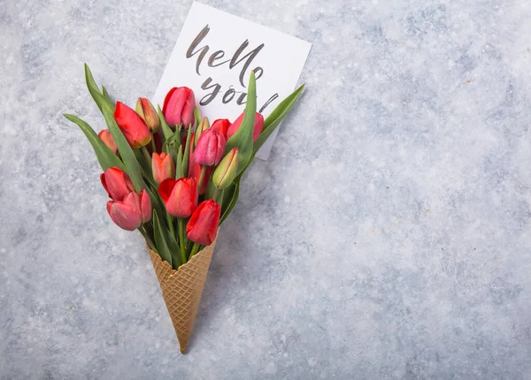 red  beautiful tulips in an ice cream waffle cone with card Hello you on a concrete background. Conceptual idea of a flower gift. Spring mood