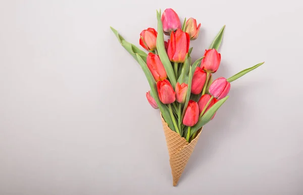 red  beautiful tulips in an ice cream waffle cone with card Womans Day on a concrete background. Conceptual idea of a flower gift. Spring mood