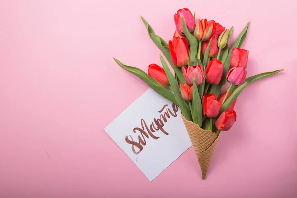 red  beautiful tulips in an ice cream waffle cone with card Womans Day on a color background. Conceptual idea of a flower gift. Spring mood