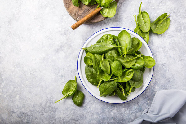 Baby spinach leaves in bowl on grey concrete background, top view, copy space. Clean eating, detox, diet food ingredient