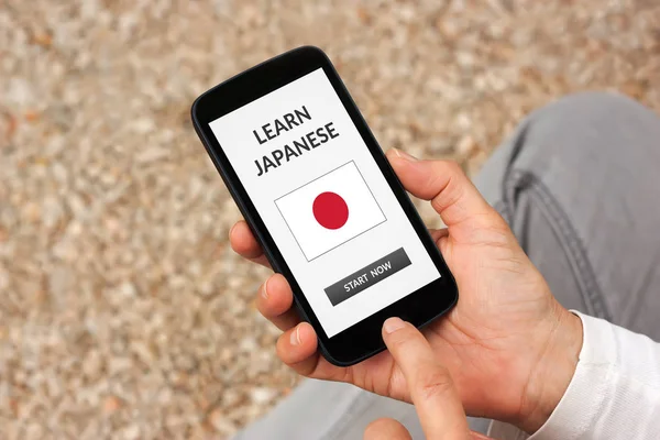 Manos sosteniendo el teléfono inteligente con aprender el concepto japonés en la pantalla — Foto de Stock