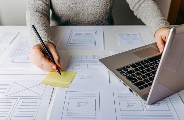Web designer working at laptop and website wireframe sketches